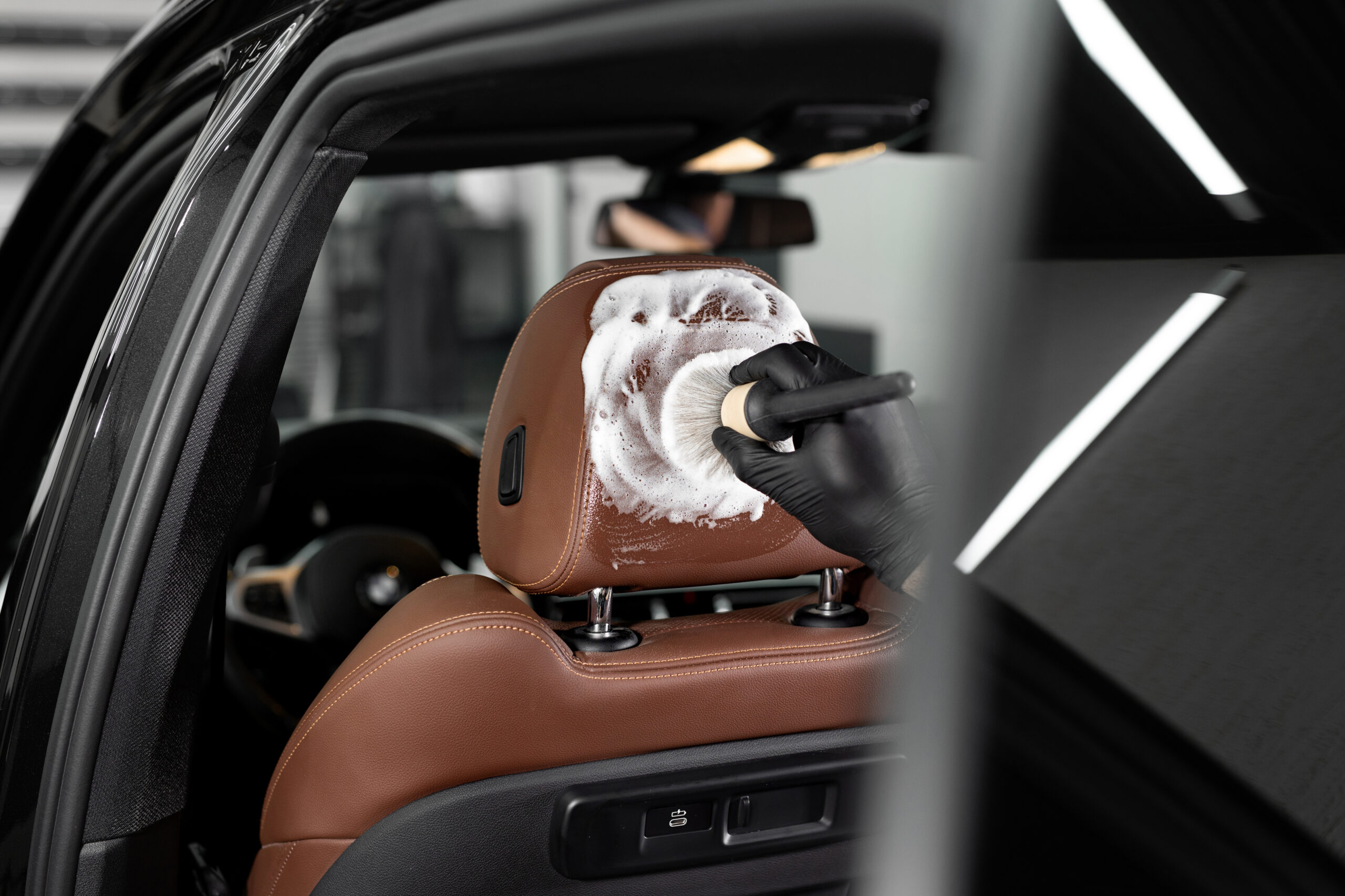 Washing with foam with a brush of the interior, leather car seats. Car detailing service.