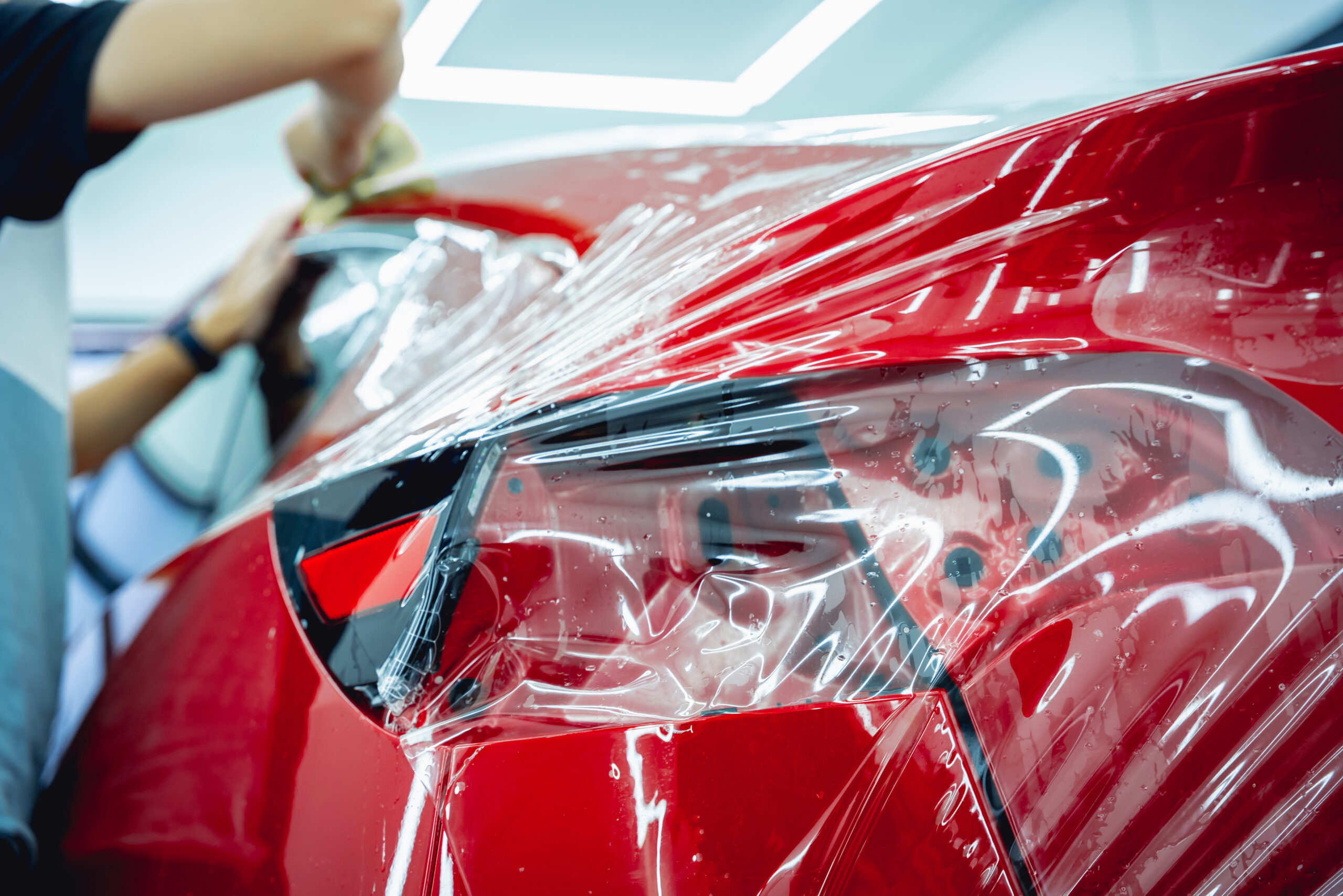 Worker in car service sprays water on the car before applying an protective film. Jakie elementy auta najczęściej zabezpiecza się folią PPF?